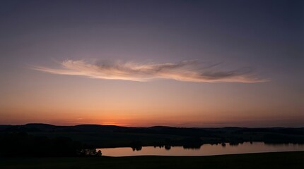 Fototapeta premium Serene Sunset Over a Calm Lake with Silhouetted Hills.