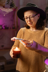 realistic witch holding voodoo doll and candle casts spell. Everyday life intertwined with traditional witchcraft, magic and mystical atmosphere. © Andrii Lysenko