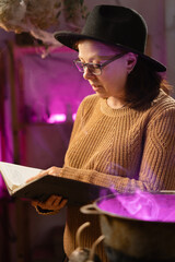 realistic witch brewing potion in cauldron. learns witchcraft from a book. Everyday life intertwined with traditional witchcraft, magic and mystical atmosphere. © Andrii Lysenko