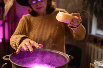 realistic witch with candle over cauldron brewing potion casting spells. Everyday life intertwined with traditional witchcraft, magic and mystical atmosphere. copy space. Halloween © Andrii Lysenko