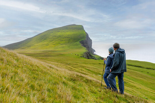 Couple hiking green hillside overlooking ocean