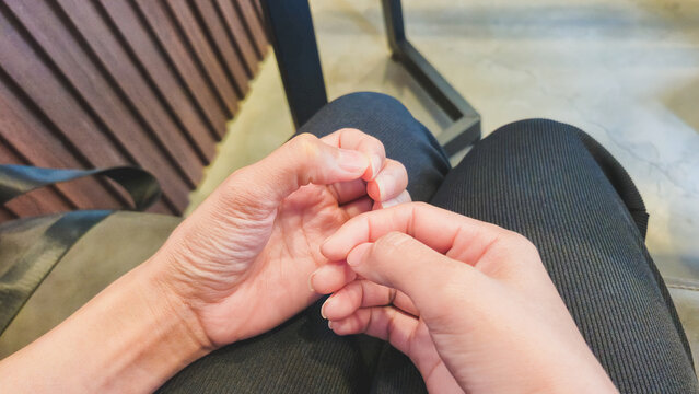Close‑up of two hands gently touching and fidgeting on dark pants with wooden panel, metal chair leg, and concrete floor background for intimate lifestyle and candid photography presentations