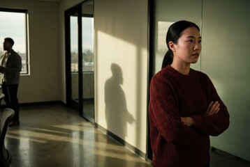 Fototapeta premium Generative AI, Serious Asian woman standing with crossed arms in office setting