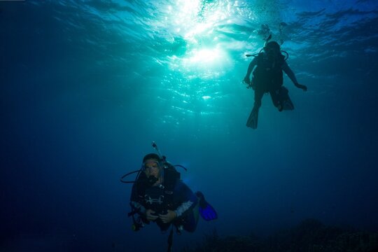 Two scuba divers beneath sunlit tropical water near Harley Reef, Guam in the western Pacific Ocean