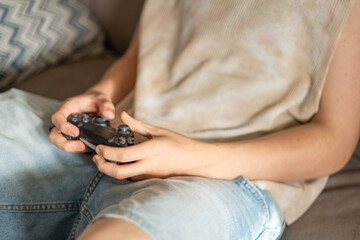 Close view of teenage hands holding black gamepad during game, gaming session lasting longer than planned, focus rare outside of game. Wide shot. Concept of teenager gaming at home © iwavephoto