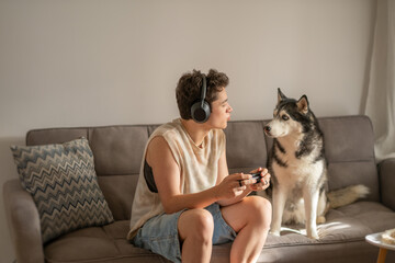 Boy pauses game and looks at his husky sitting close on sofa, distraction stronger than any game level, frame for gaming content. Wide shot. Concept of distraction that beats any game © iwavephoto