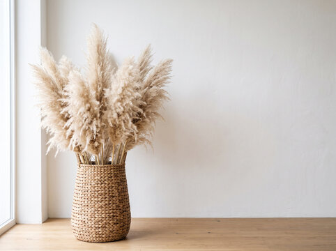 Minimalist boho decor with pampas grass in a woven rattan basket on a wooden table against a white wall with copy space