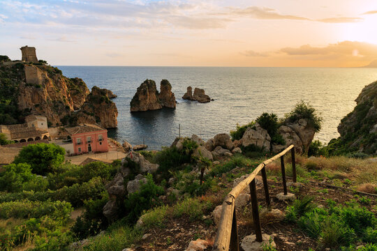 Scenic coastal landscape with a historic stone tower and villa at golden hour in Sicily