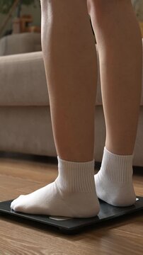 Woman feet in white socks stepping on digital electronic scales to check weight on wooden floor.