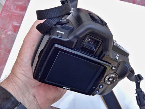 Hand holding Sony DSLR camera displaying screen