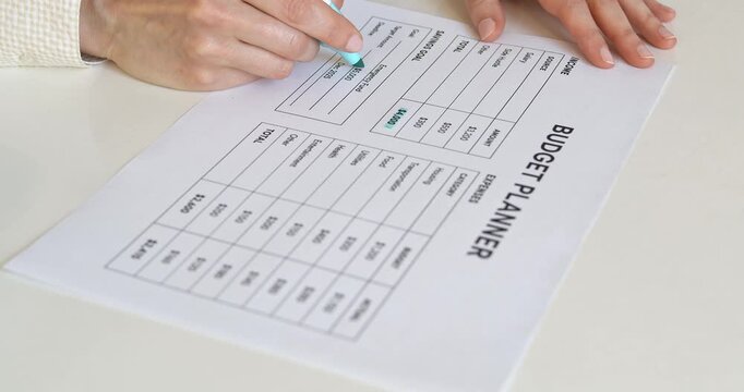 Woman hand writing total expenses amount with blue marker on paper budget planner.