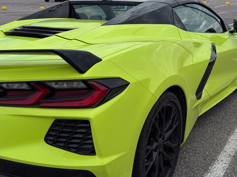 Rear view of yellow Chevrolet Corvette Stingray C8 Convertible supercar. American sports car with black spoiler, led taillight, side air intake and alloy wheel parked, automotive vehicle concept.