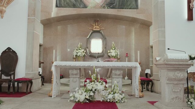 Stone church altar with white flower arrangements a red carpet and a gilded tabernacle prepared for a wedding ceremony in Balasar Portugal.