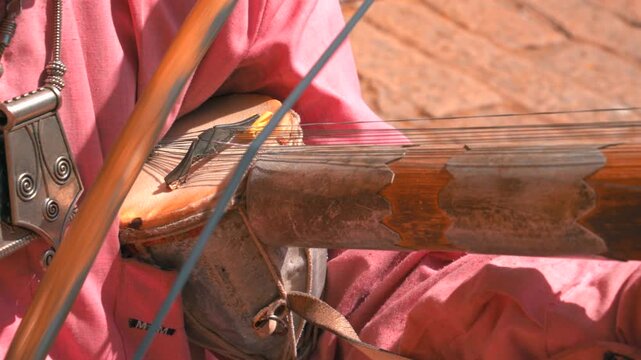 Cinematic macro static shot of a street artist playing the ancient ravanahatha bowed string instrument in Jaisalmer, Rajasthan, India.