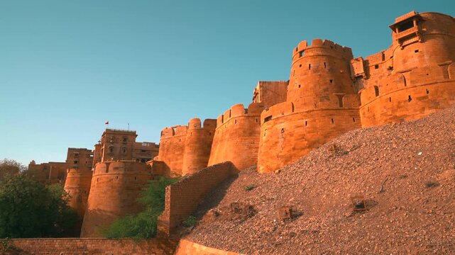 Cinematic low angle static shot of massive golden sandstone bastions and fortification walls of Jaisalmer Fort standing on a rocky hill in Rajasthan, India.