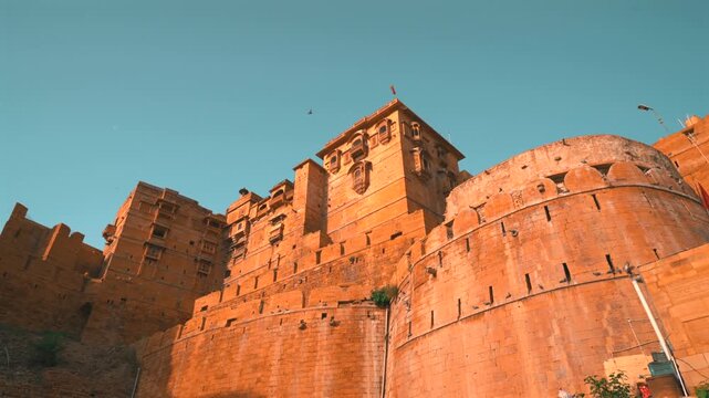 Cinematic pan right low angle shot of the massive stone bastions and multi-tiered fortification walls of Jaisalmer Fort, Rajasthan, India.