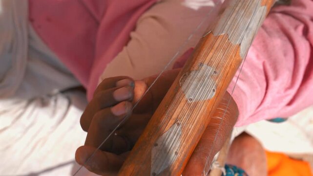 Cinematic close up shot of a local Indian folk musician playing a traditional wooden stringed instrument in Jaisalmer, Rajasthan, India.