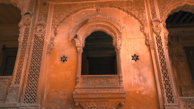 Cinematic pull out shot of an intricately carved sandstone jharokha balcony and jaali screen on a traditional haveli in Jaisalmer, Rajasthan, India.