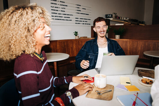 Friends laughing over coffee and laptop in cafe