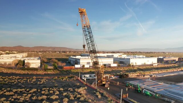Wide aerial panning shot of an industrial crawler crane operating at a desert construction site in Palmdale, California. 4K