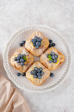 Danish puff pastry cakes with custard cream and fresh berries, sprinkled with powdered sugar on a white plate on a concrete background.