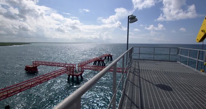 Static high-angle wide shot looking out from the elevated steel platform over the red walkways and mooring dolphin structures surrounded by blue ocean water at Coastal Petroleum terminal in San Pedro