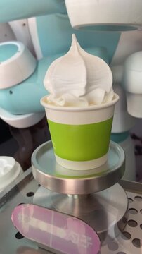 Robotic arm holding and preparing a soft serve ice cream cup, automated dessert vending machine and futuristic food technology concept, real-time footage