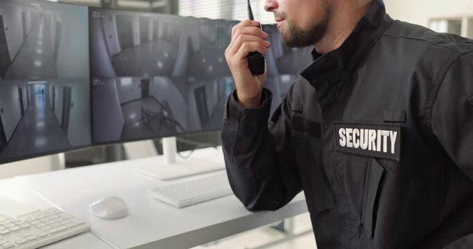 Security guard monitors CCTV surveillance cameras with radio. An officer checks live feeds for safety response at a monitoring workstation. Security operations and protection concept.