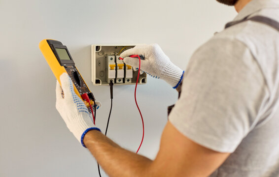Electrician testing circuit breaker panel wiring. Technician uses a multimeter to inspect electrical wiring during routine residential maintenance. Electrical safety and repair concept.