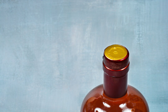 A high angle view of a glass bottle neck sealed with a red foil capsule and a golden top on a gray textured background with copy space.