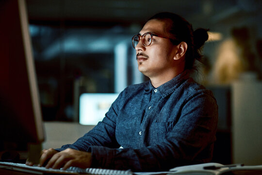 Typing, man and computer in office at night for urgent bug fix, troubleshoot software and overtime. Glasses, developer and tech at agency for system maintenance, app development and project deadline