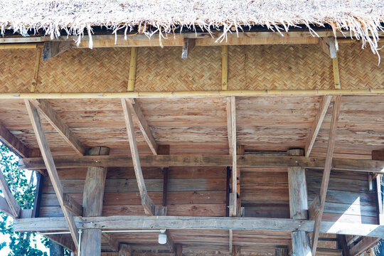 Wooden structure and thatched roof of a traditional stilt house, A low-angle shot showing the wooden beams, bamboo woven wall, and straw thatched roof under the ceiling of a rustic countryside hut.