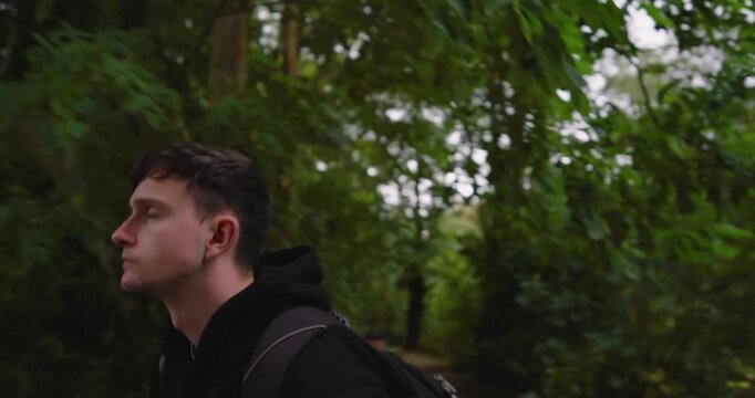 Young man with backpack jogging through lush green park, focused and determined