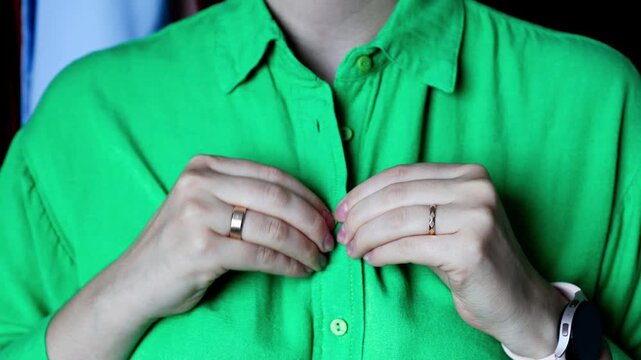 Close-up of hands unbuttoning a vibrant green linen shirt.