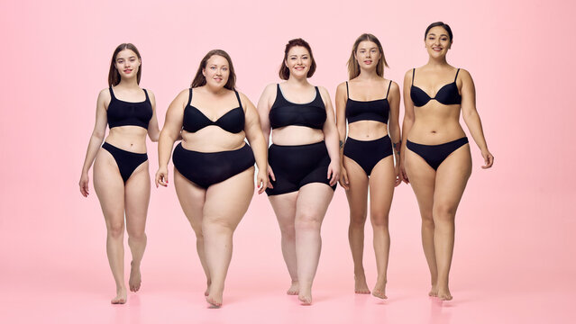 Empowered female group walks boldly forward across pink studio. Inclusive fashion, equality, collective strength concept.