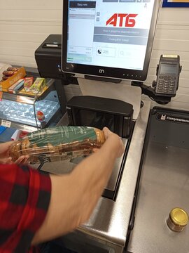 Zvyagel, Ukraine - September 16, 2026: Customer uses a self-checkout counter at a Ukrainian ATB supermarket, scanning a loaf of bread before paying by card at the automated station.