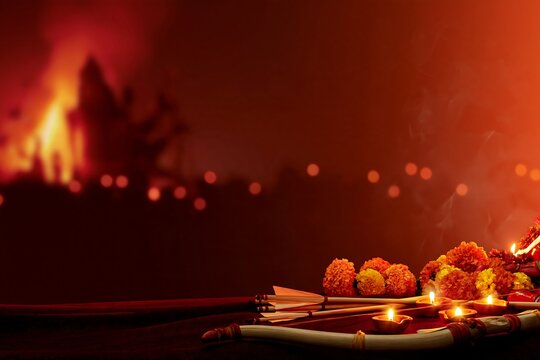 Bow and arrows with glowing oil lamps and marigold flowers on red background, Dussehra and Vijayadashami festival concept with copy space for holiday greetings