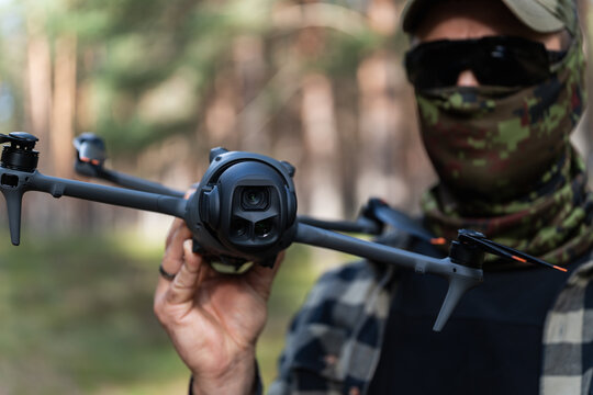 Tactical drone instructor in camouflage balaclava holding reconnaissance quadcopter with multi camera telephoto zoom system during outdoor forest operations training