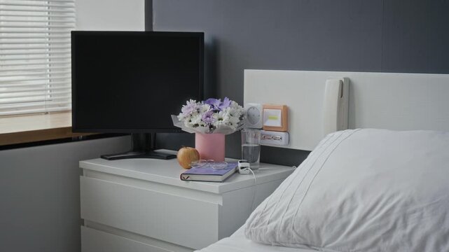 Empty hospital ward featuring made bed, bedside table with flowers, monitor and personal belongings. Clip ideal for medical advertising, healthcare documentaries and clinic promotional projects