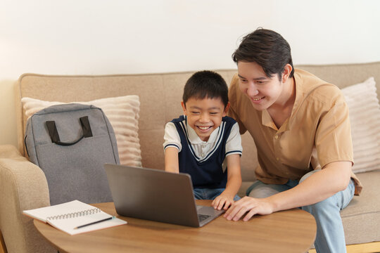 Happy Asian father and son learning on laptop together at home for back to school