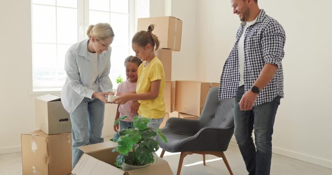 Happy family moving boxes into a new home. Parents and children arrange furniture and plants in a bright apartment, enjoying a playful relocation and fresh start. New beginnings start here today.