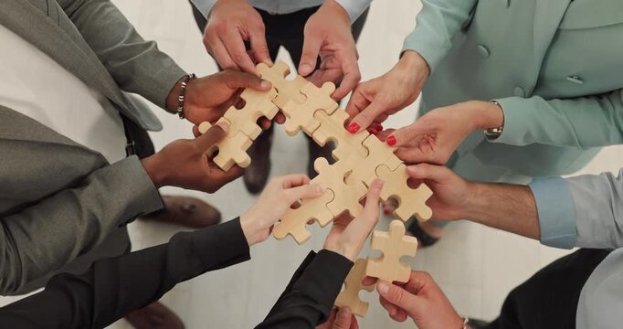 Business team hands assemble puzzle pieces together. Top view shows colleagues connecting wooden parts for collaboration, partnership, and planning. Teamwork creates unified business outcomes.