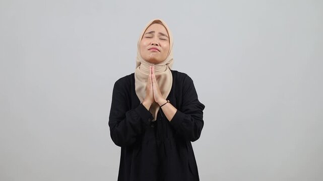 Asian muslim woman keeps palms in pray gesture looks with begging expression asks for offer has imploring look.