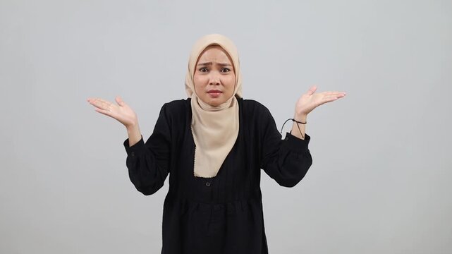 Confused young asian muslim woman standing between two choice and showing puzzled face expression gesture