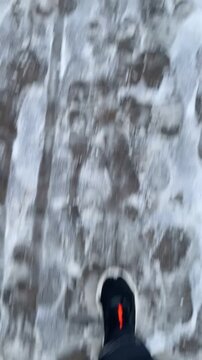 Winter walk. Snowy icy pavement boots walking commute. handheld viewpoint captures black boot stepping. Vertical POV taken on mobile device.