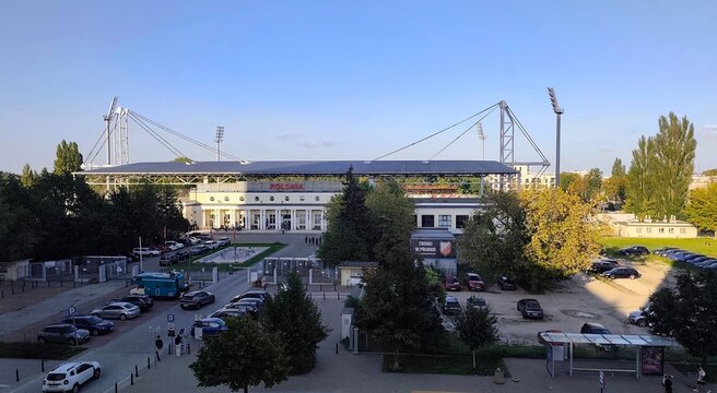 Exterior view of Polonia Warsaw municipal stadium in Warsaw, Poland, featuring its historic neoclassical facade, cable-stayed roof, parking area and trees in the Śr&oacute;dmieście district.