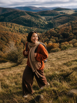 Vertical portrait of a young woman hiking in autumn mountains. Happy female hiker with backpack walking on a grassy hill. Active outdoor lifestyle