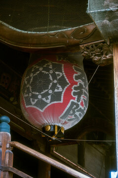 A large, traditional chochin (Japanese paper lantern) hanging underneath the wooden eaves of a temple structure 