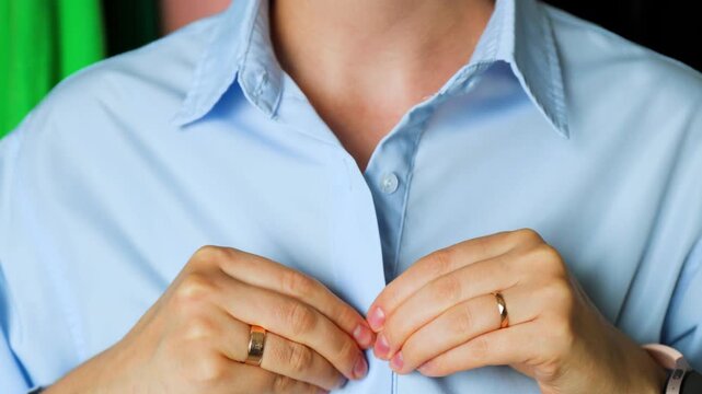 Close-up of a person unbuttoning a blue cotton shirt.