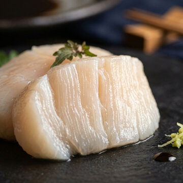 Fresh raw scallop meat served on a dark stone plate with wasabi and soy sauce.